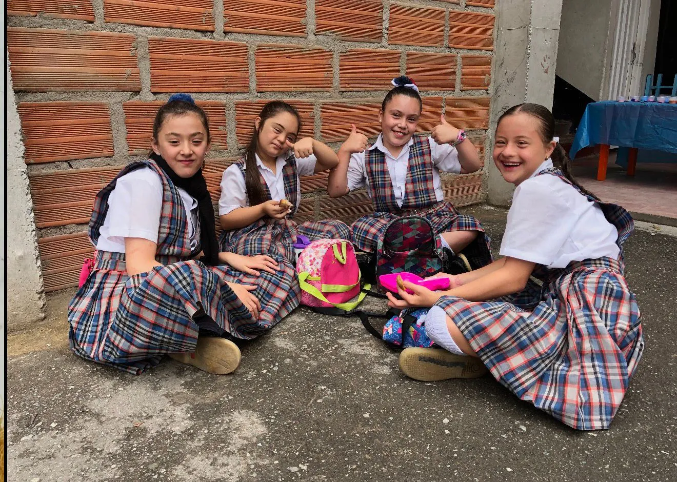 Cuatro estudiantes de primaria con el uniforme de gala conversan y ríen sentadas juntas durante el descanso