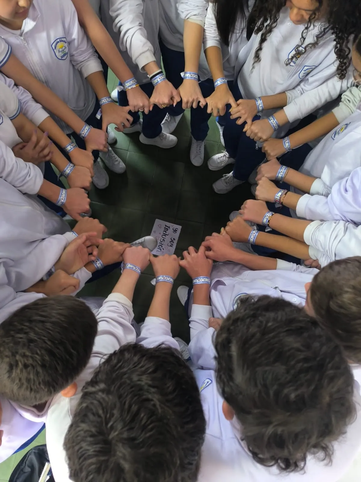 Estudiantes de Senderos sentados en círculo en el patio, tomados de las manos y con la manilla del colegio en la muñeca, alrededor de un cartel escrito a mano que dice «Yo soy inclusión»